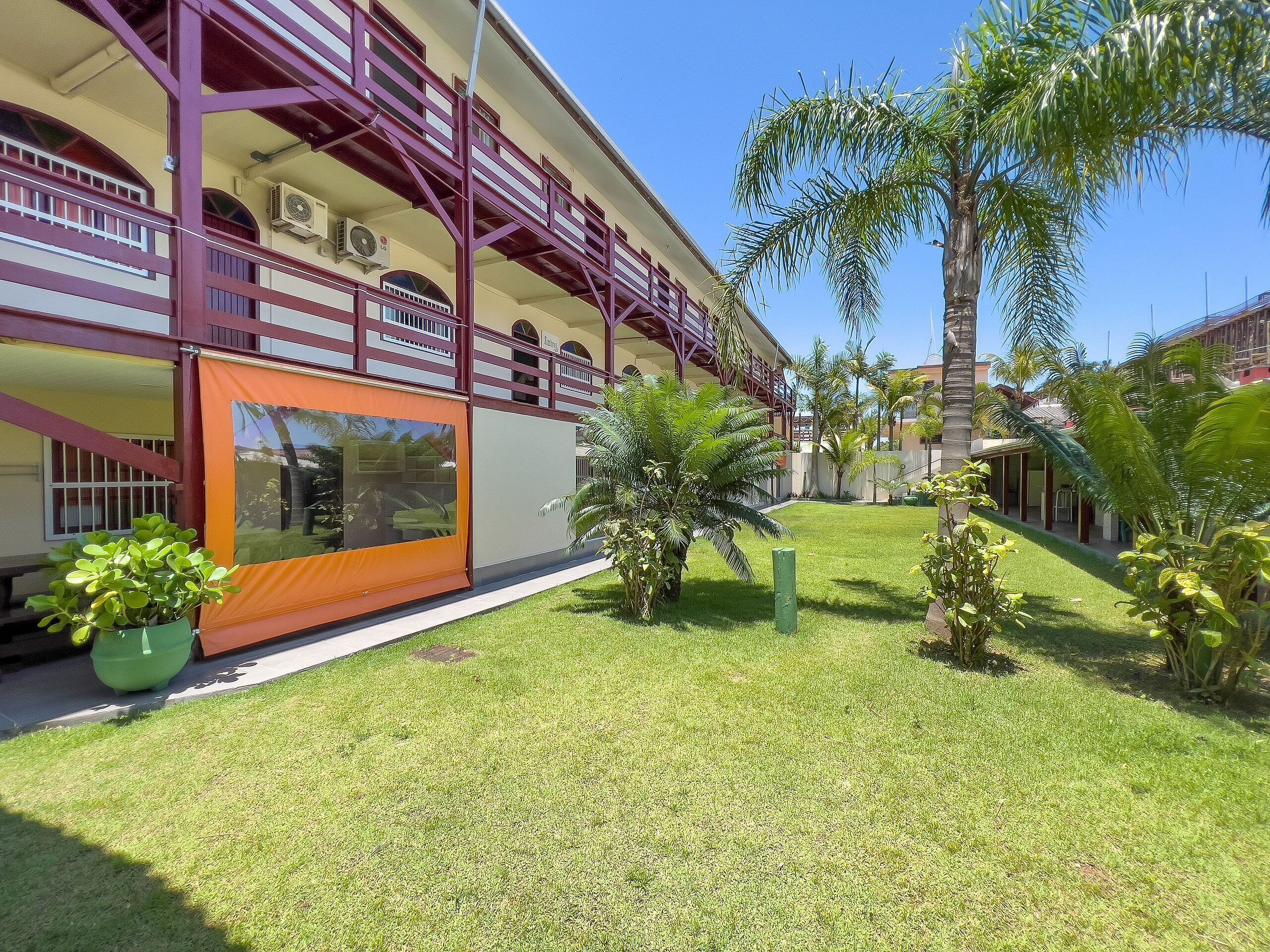 A hotel with a covered outdoor area, a well-maintained lawn, and several palm trees.