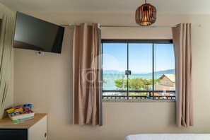 A hotel room with a large window, a flat-screen TV, and a small table with snacks. - Suíte 1 Ala pôr sol Residencial Solavir (Bombinhas)