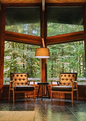 A room with large windows, two upholstered chairs, a floor lamp, and a small table.