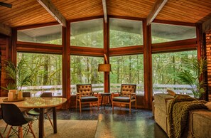 A room with large windows, a dining table, two chairs, a sofa, and a lamp.