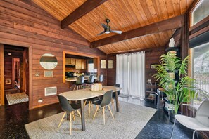 Un interior de madera con una zona de comedor, un ventilador de techo y un ventanal grande.