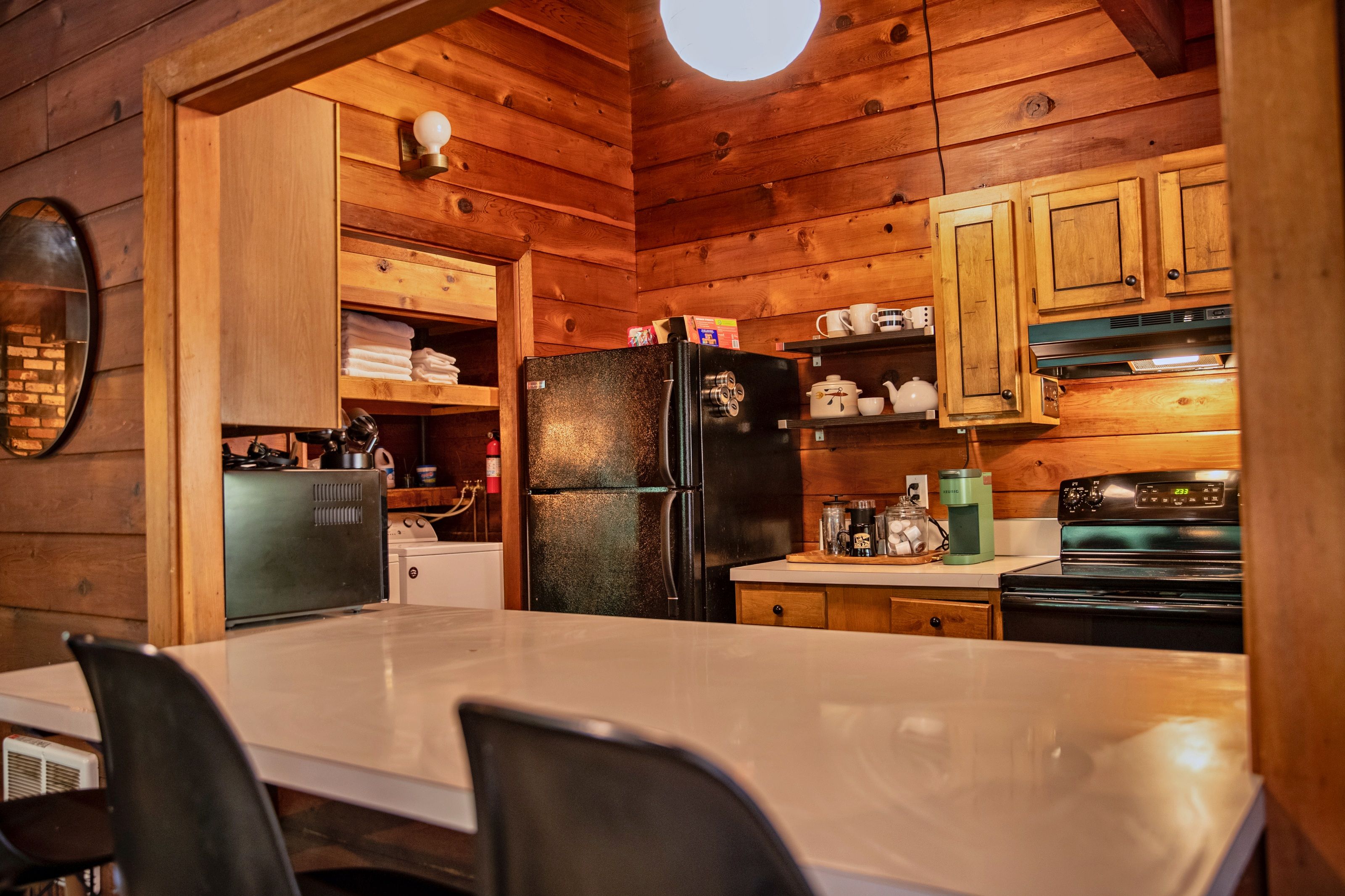A wooden cabin interior with a kitchen area featuring a refrigerator, stove, and wooden cabinets.