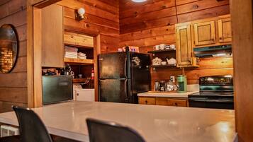 A wooden cabin interior with a kitchen area featuring a refrigerator, stove, and wooden cabinets.