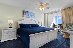 A hotel room with a bed, nightstands, a ceiling fan, a painting, and a view of the outdoors.
