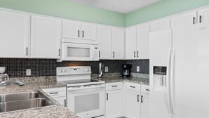 A kitchen with white cabinets, a microwave, a stove, a sink, and a refrigerator. - Oceanfront Views w/ 7 Beds, Pools, Lazy River, Gym (North Myrtle Beach)