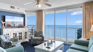 A room with a large window, a ceiling fan, and a TV on a cabinet. - Oceanfront Views w/ 7 Beds, Pools, Lazy River, Gym (North Myrtle Beach)