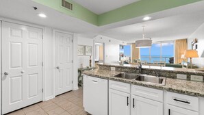 A modern kitchen with white cabinetry, granite countertops, and a large window offering a view of the ocean. - Oceanfront Views w/ 7 Beds, Pools, Lazy River, Gym (North Myrtle Beach)