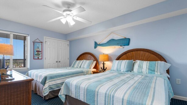 A bedroom with two beds, a ceiling fan, a fish wall decoration, and a lamp on a nightstand. - Oceanfront Views w/ 7 Beds, Pools, Lazy River, Gym (North Myrtle Beach)