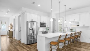 A modern kitchen with white cabinetry, stainless steel appliances, and a central island with bar stools. - Sandy Toes Retreat with LSV and Woodlands (Miramar Beach)