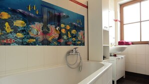 A bathroom with a large mural of marine life, a bathtub, a white sink, and a window.