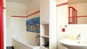 A bathroom with a bathtub, a sink, and a mirror. There is a red towel rack and a red door.