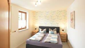 A bedroom with a bed, two bedside tables, a window, and a wall with a floral pattern.