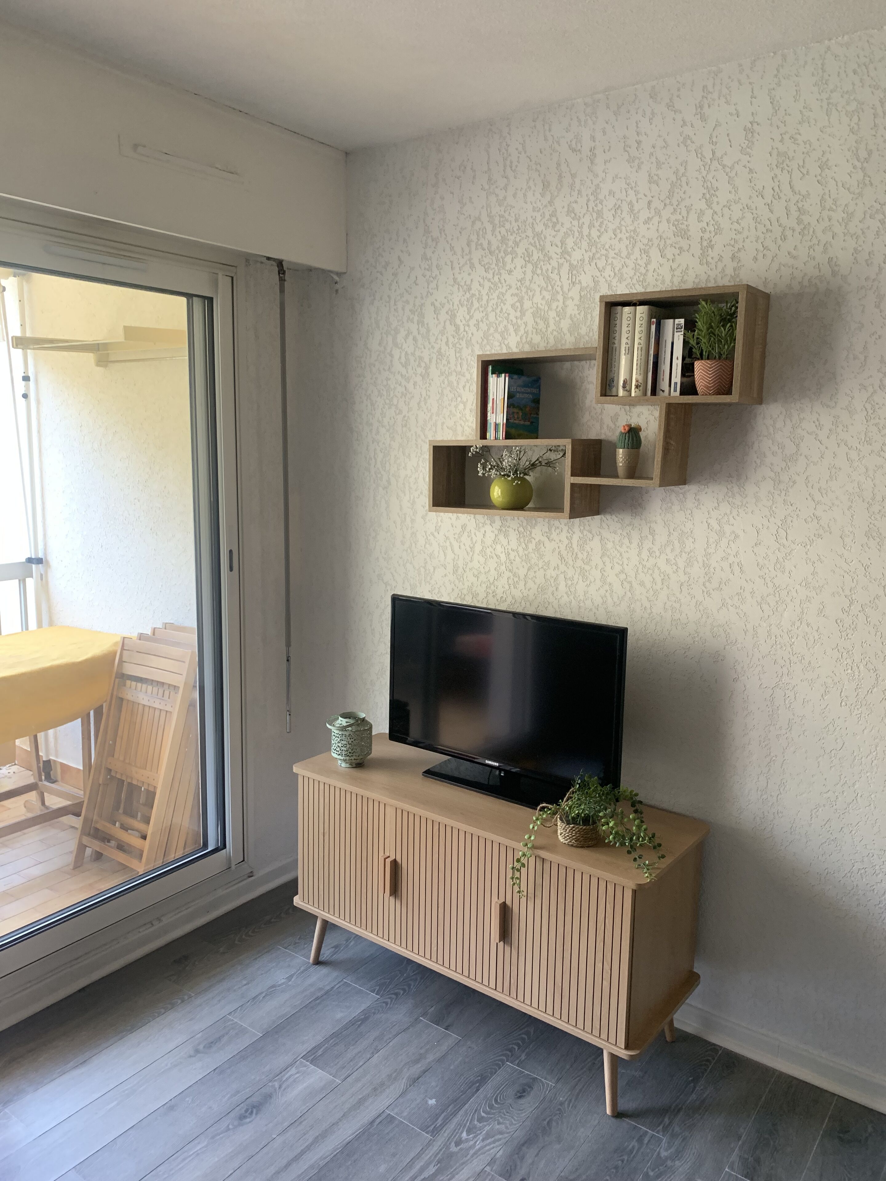 Un salon moderne avec un téléviseur posé sur un meuble en bois, une porte-fenêtre coulissante et un mur décoré d’un motif.