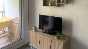 Un salon moderne avec un téléviseur posé sur un meuble en bois, une porte-fenêtre coulissante et un mur décoré d’un motif.