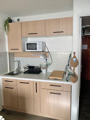 A kitchen with wooden cabinets, a microwave, a sink, and a countertop with kitchen utensils. - Cozy apartment 500 m from the beach, perfect for a family with 2 children (Saint-Mandrier-sur-Mer)