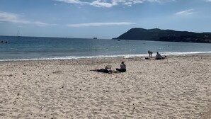 Une plage de sable avec quelques personnes et des bateaux sur l’eau.