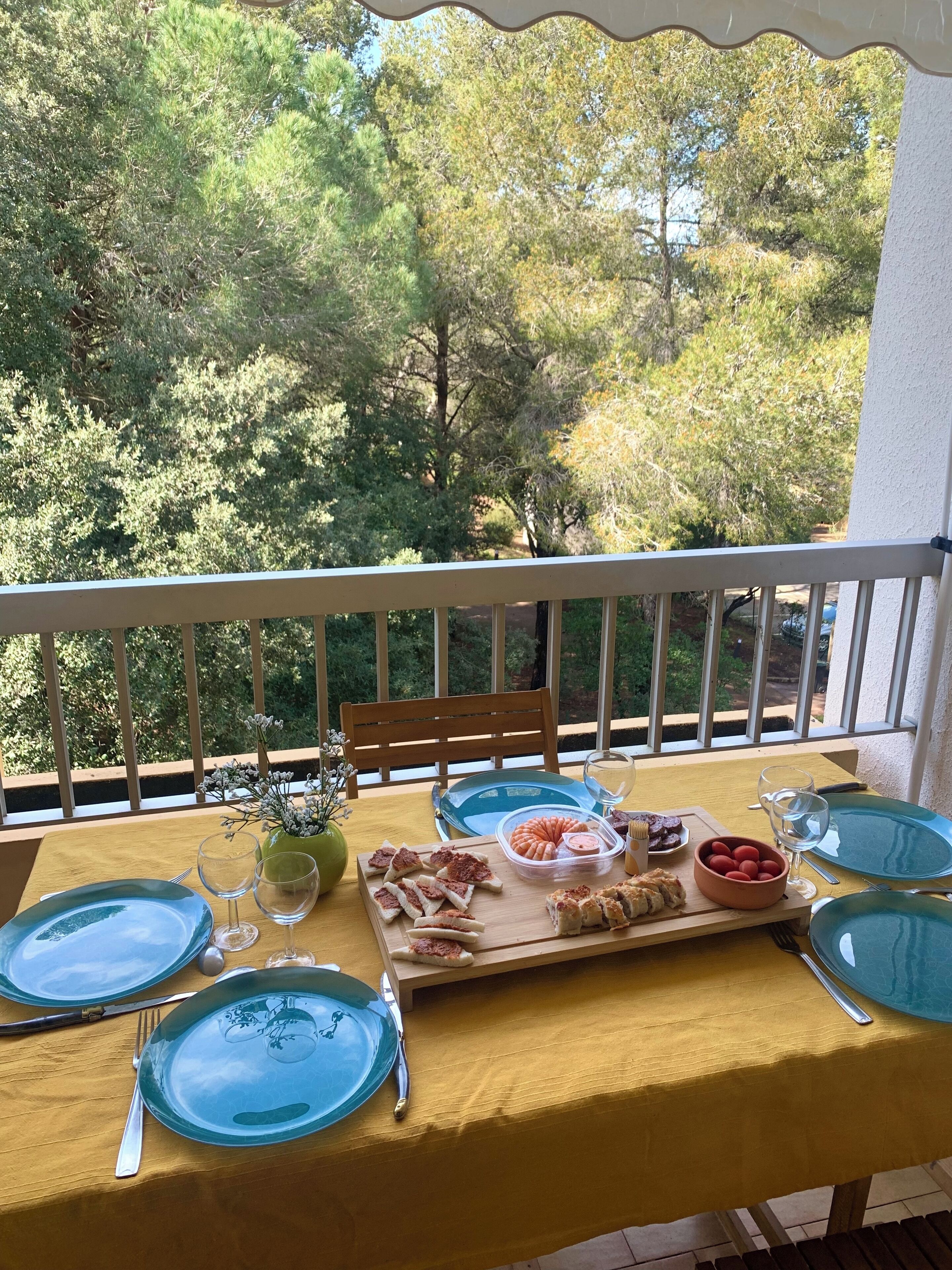 A balcony table set with blue plates, cutlery, and a variety of snacks and drinks.