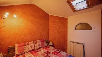 A bedroom with a wooden bed, a quilt with a snow pattern, a skylight, and a radiator.