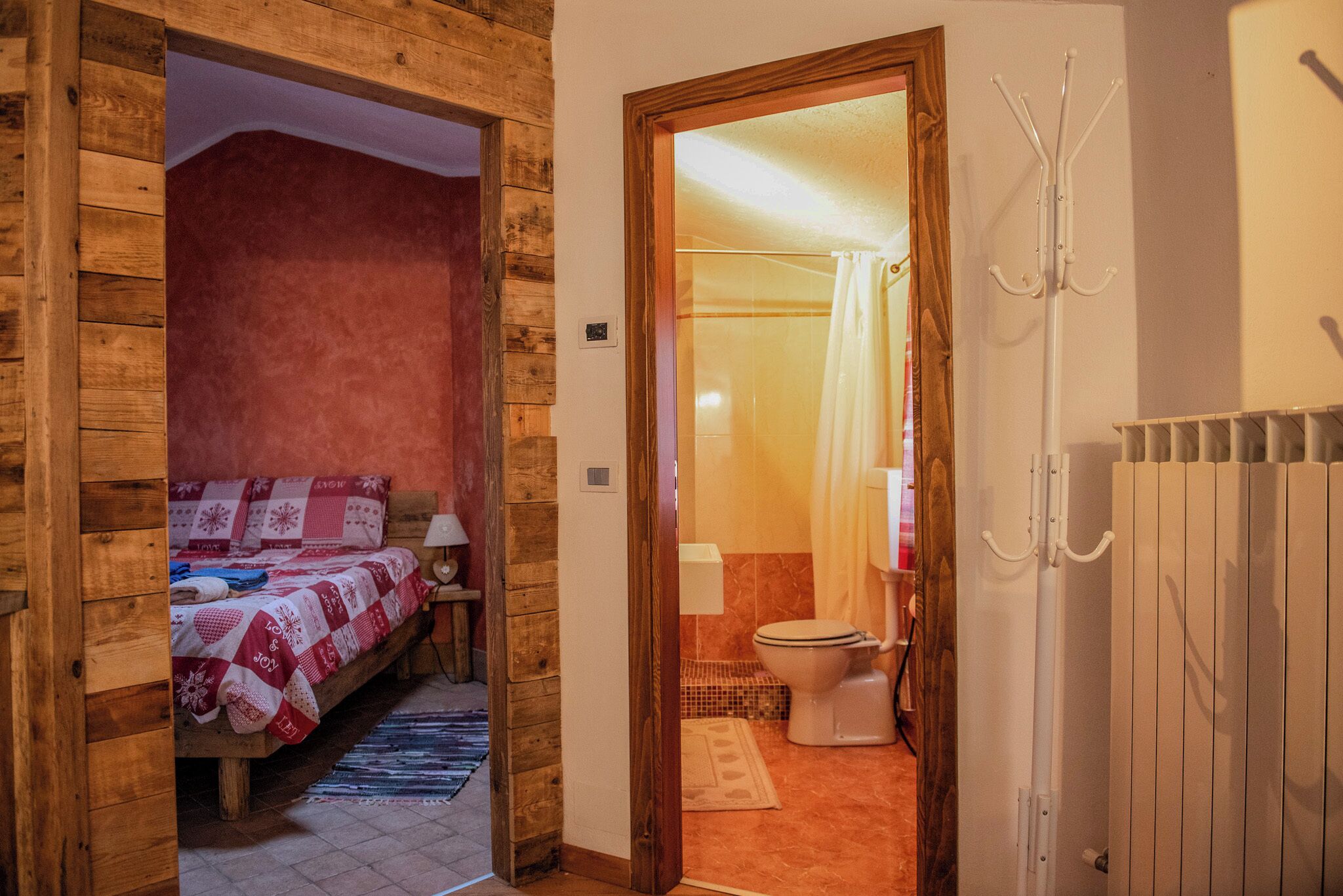 A wooden room with a bed, a nightstand, and a bathroom visible through an open door.