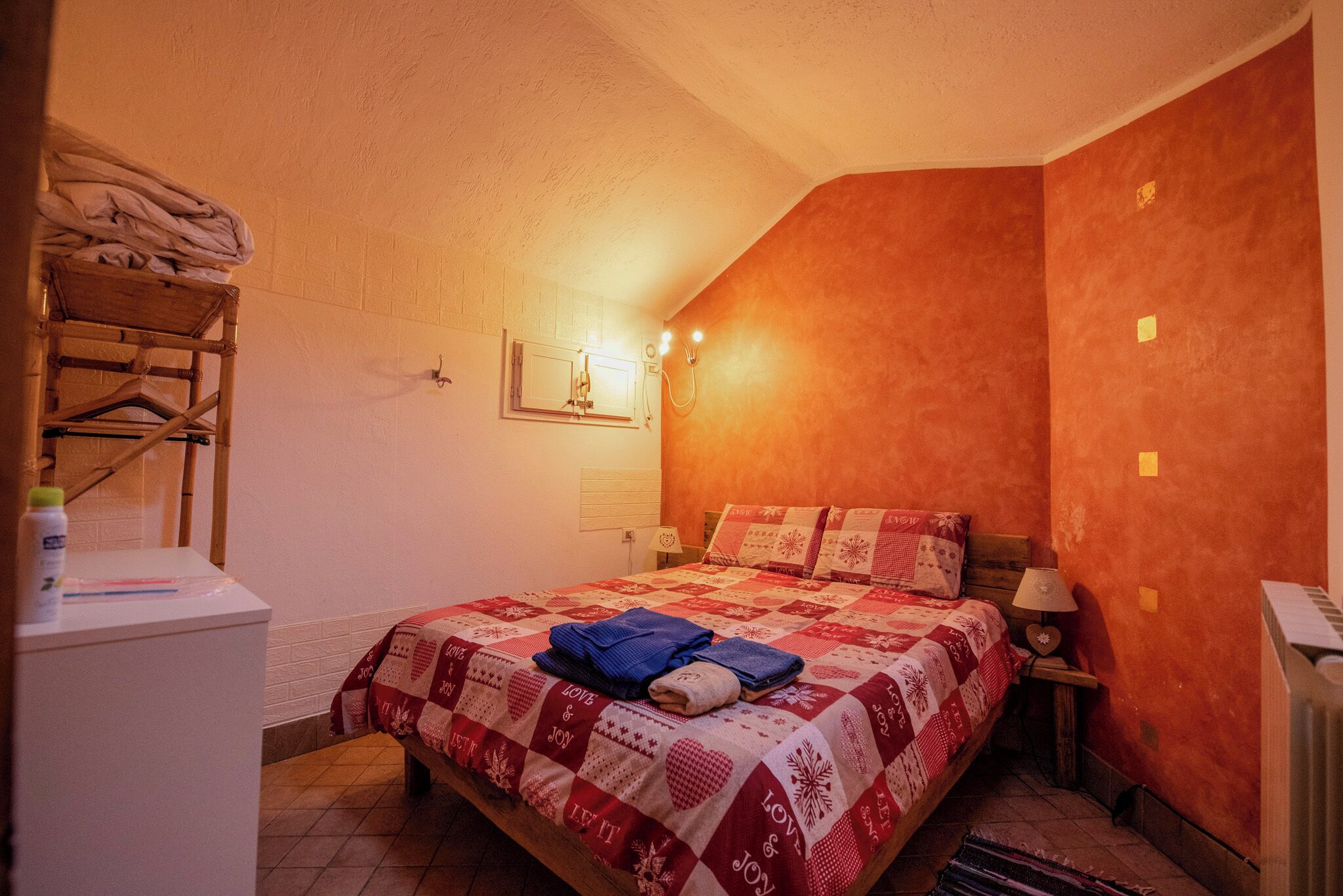 A bedroom with a bed, a wooden chair, a nightstand, and a wall-mounted light fixture.
