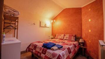 A bedroom with a bed, a wooden chair, a nightstand, and a wall-mounted light fixture.