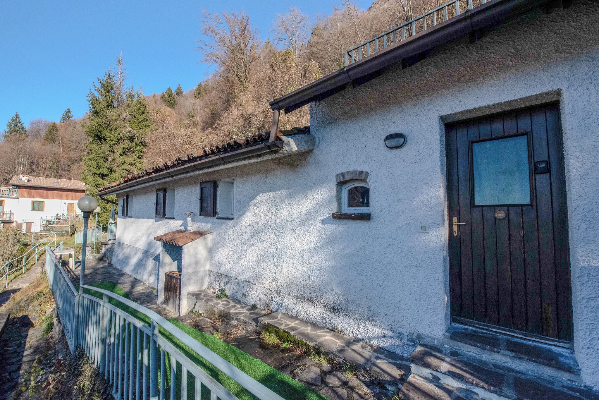 Ein weißes Gebäude mit einer dunkelholzigen Tür, einem kleinen Fenster und einem steinbelagten Weg, der zum Eingang führt.