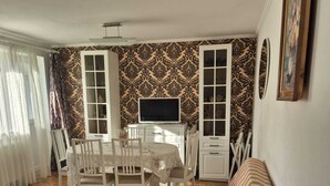 Un salon confortable avec un téléviseur, une table à manger avec des chaises, un papier peint à motifs et un banc.