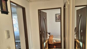 Une chambre d’hôtel avec un plancher en bois, un lit recouvert d’une couverture orange, un grand miroir et une porte donnant sur une autre pièce.