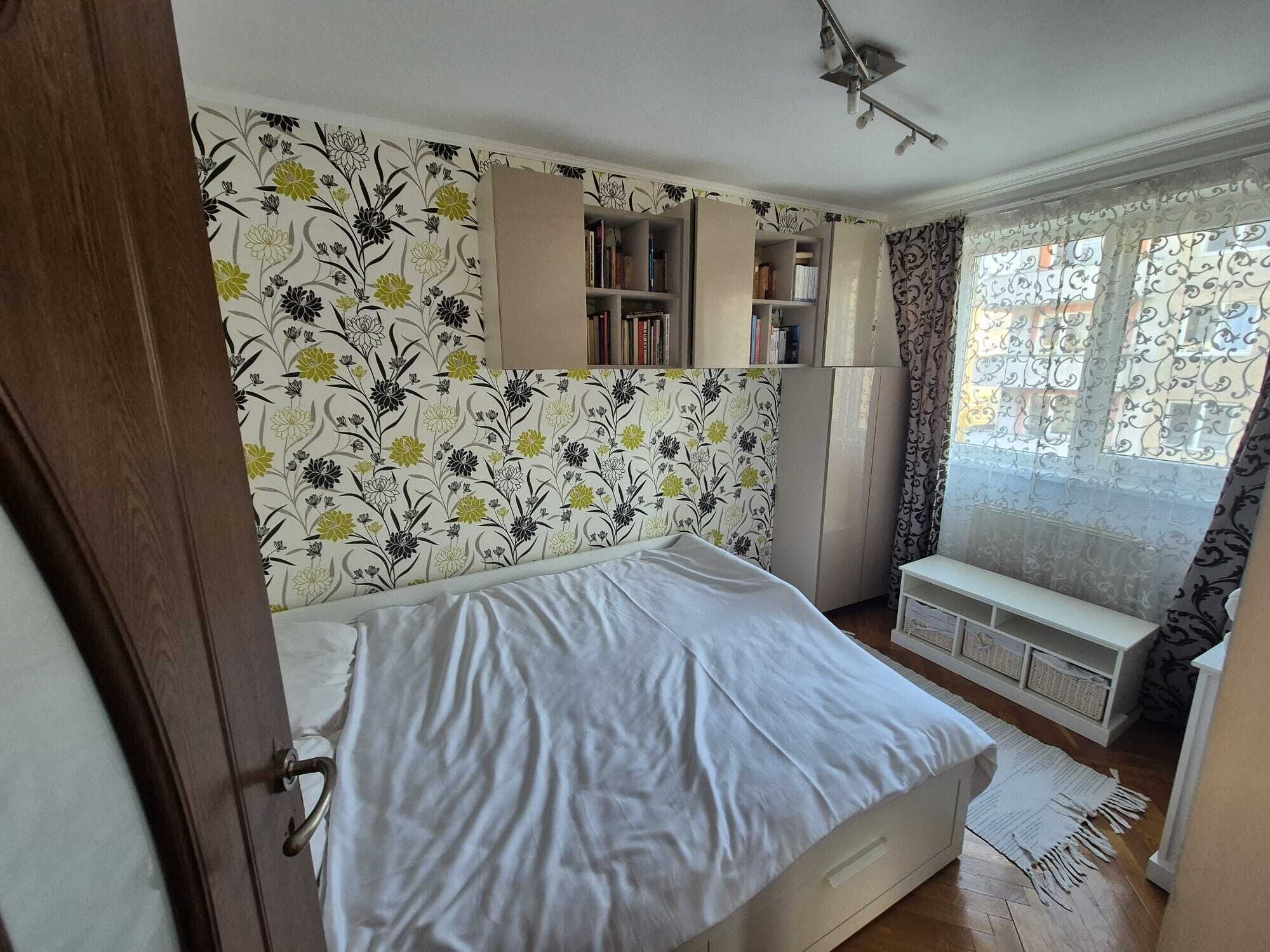 A bedroom with a bed, a wardrobe, a window with curtains, and a bookshelf.