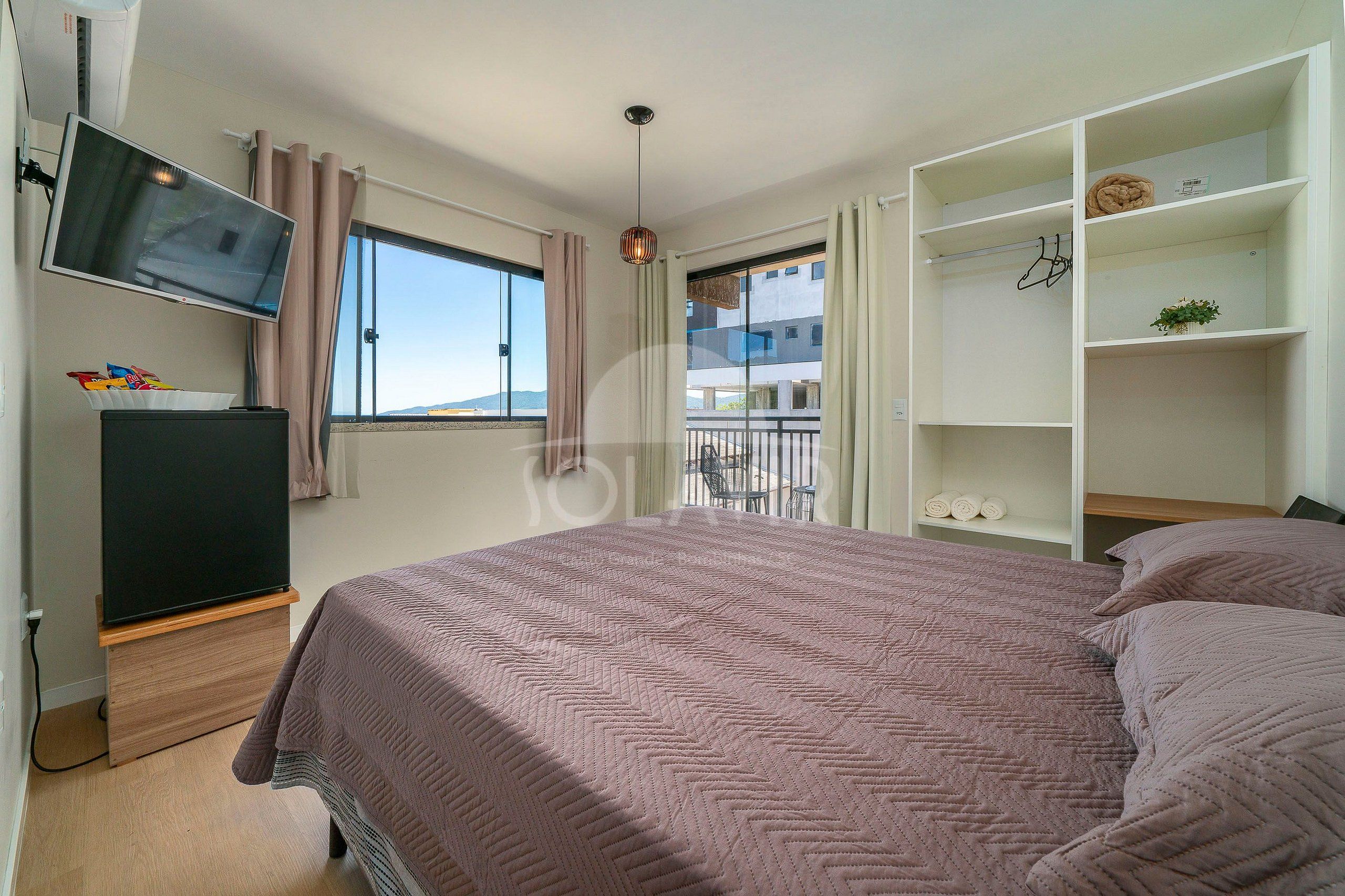 Un dormitorio con cama, televisión, armario y ventana con cortinas.