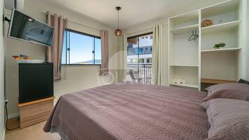 Un dormitorio con cama, televisión, armario y ventana con cortinas.