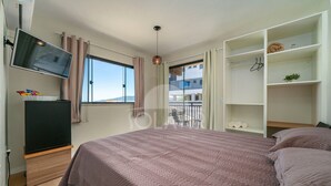 A bedroom with a bed, a TV, a wardrobe, and a window with curtains. - Suíte 2 Ala pôr sol Residencial Solavir (Bombinhas)