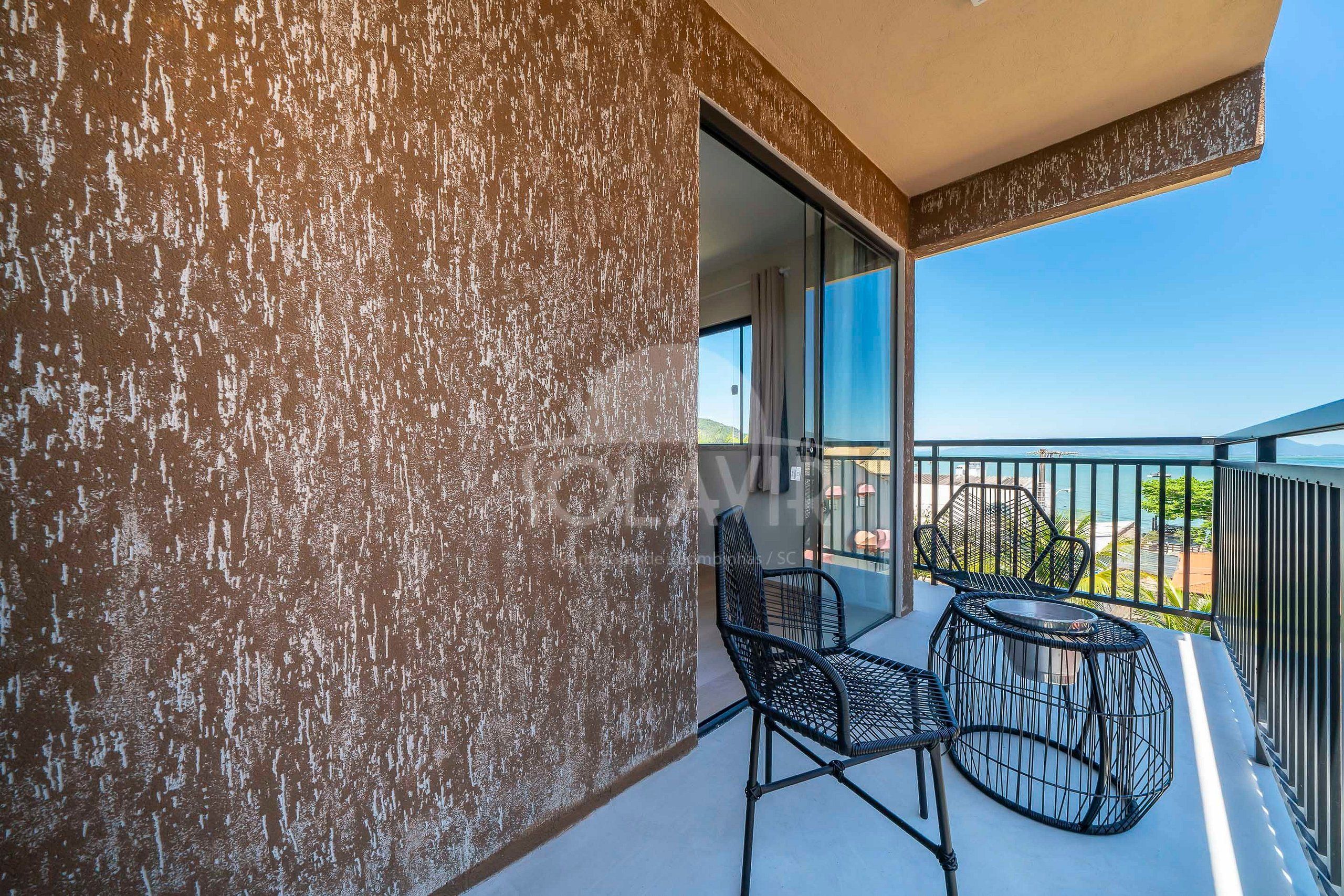 A balcony with two chairs and a table, a textured wall, and a clear view of the sky and landscape.