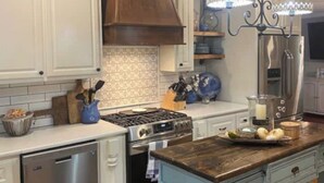 Una cocina con armarios blancos, techo de madera, electrodomésticos de acero inoxidable e isla azul con una cesta.