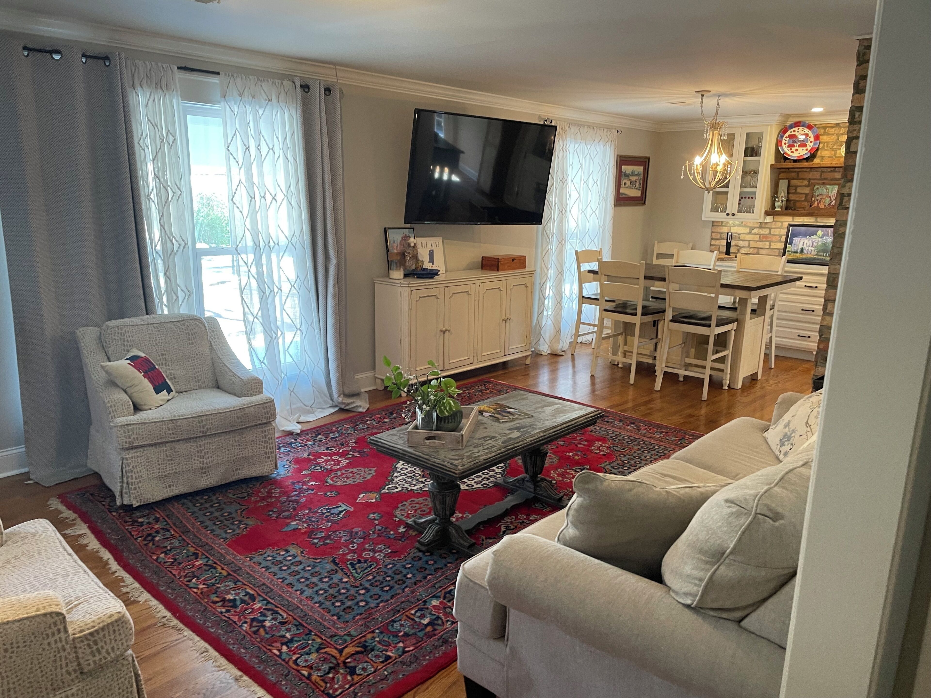 A living room with a sofa, armchair, and coffee table, a dining area with chairs and a table, and a TV mounted on the wall.