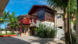 A two-story building with a red balcony, a covered walkway, and a tiled patio area. - Suíte 3 Ala pôr sol Residencial Solavir (Bombinhas)
