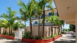 A courtyard with palm trees, a building with balconies, and a paved walkway. - Suíte 3 Ala pôr sol Residencial Solavir (Bombinhas)
