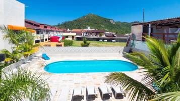 A swimming pool with lounge chairs, surrounded by palm trees and a view of a hillside.