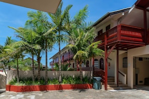 A building with a red balcony, a staircase, and a garden with palm trees.