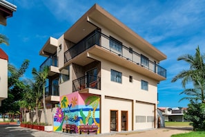 A multi-story building with balconies, a colorful mural, and palm trees.