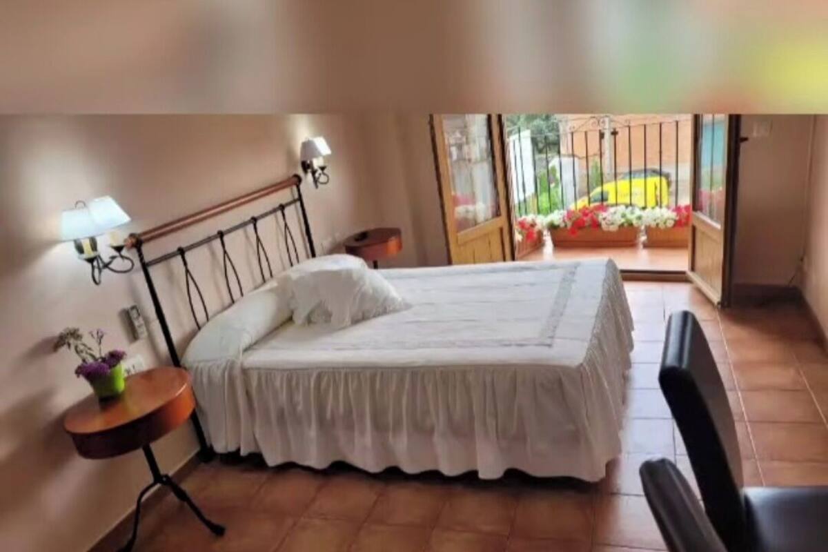 A bedroom with a bed, a small table with a lamp, and a view of a balcony with flowers.