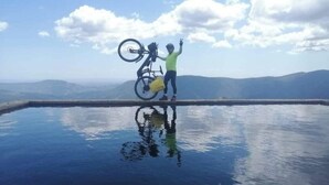 A person standing on a reflective surface with a bicycle, surrounded by a mountainous landscape. - Hotel Rural Cristania (Caminomorisco)