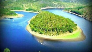 An aerial view of a lush green island surrounded by a large body of water, with hilly terrain in the background. - Hotel Rural Cristania (Caminomorisco)