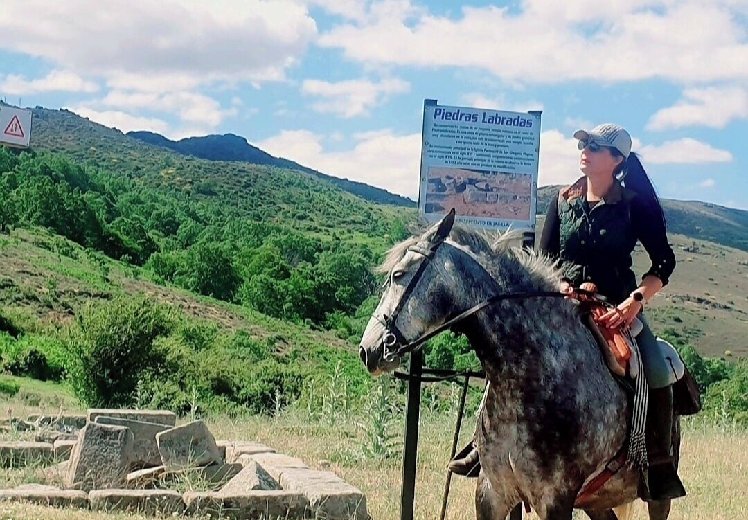 Una persona montando a caballo en un entorno natural, con un cartel al fondo.