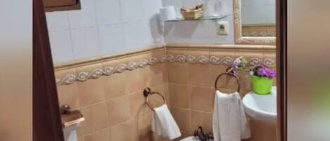 A bathroom with white tiles, a bidet, a toilet, and a sink with a mirror above it.