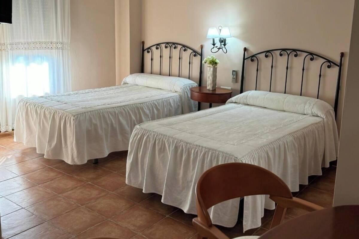 A hotel room with two beds, a small table, a chair, and a lamp.