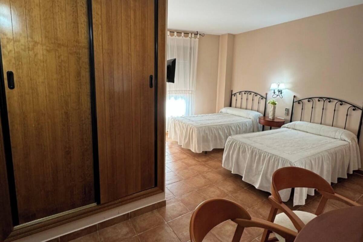 A hotel room with two beds, a wooden wardrobe, a dining table, and a chair.