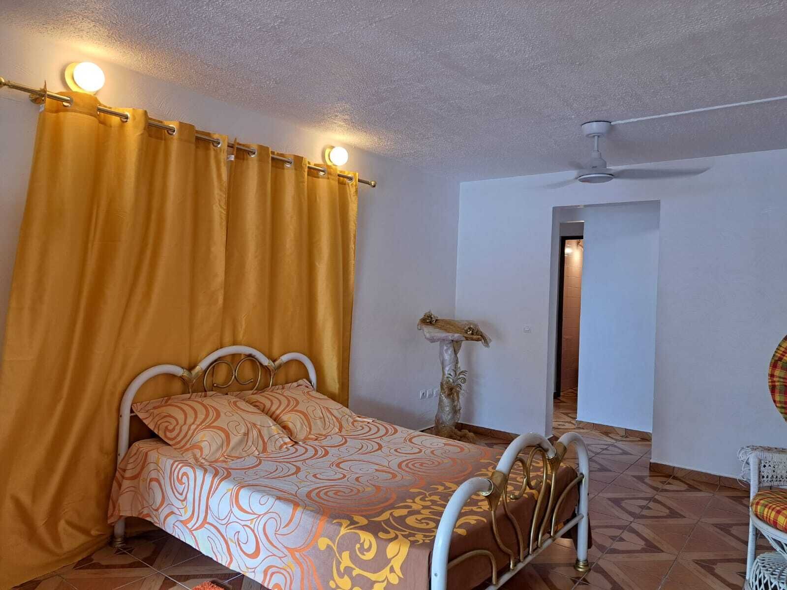 A bedroom with a bed, curtains, a ceiling fan, and a chair.