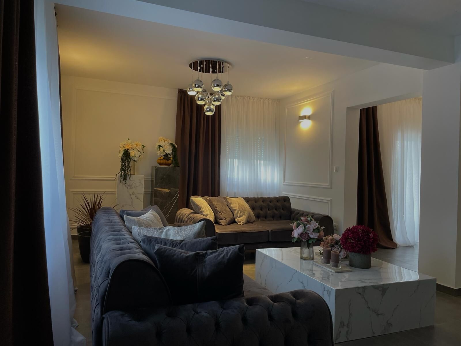 A modern living room with a dark-colored sofa, a marble coffee table, and a decorative chandelier.