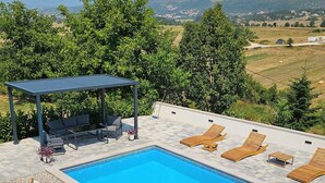 A swimming pool with lounge chairs and a covered seating area, surrounded by greenery and a view of distant hills. - Charming Holiday home with private pool,teniss field WiFi... Imotski,Croatia (Gornji Vinjani)